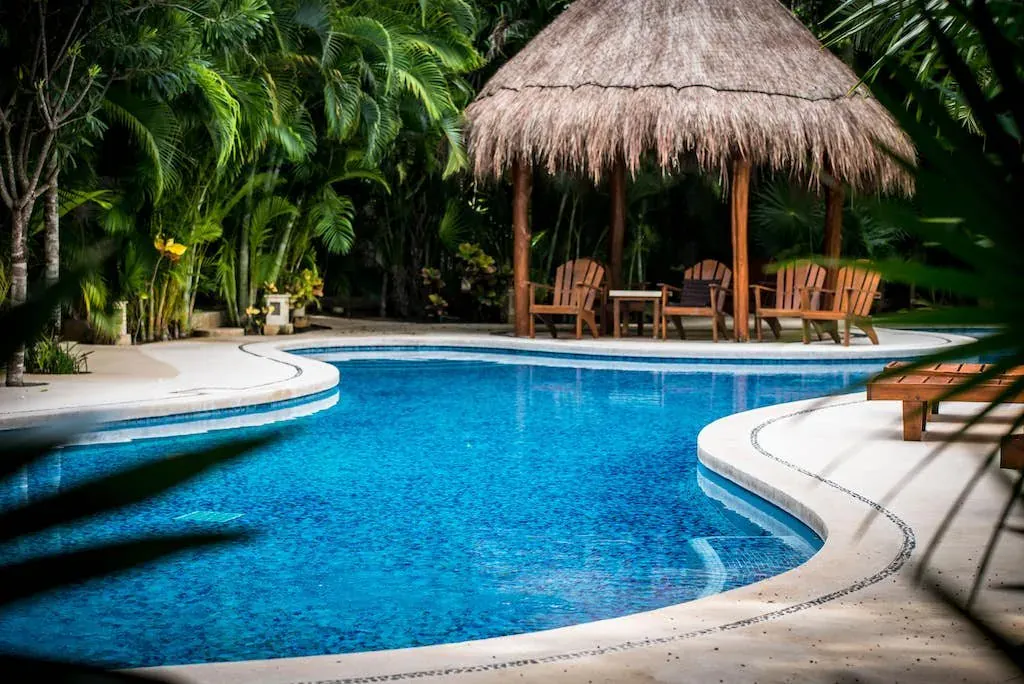 Shaded pool with a thatched palapa and wooden loungers in a jungle garden in Aldea Zama
